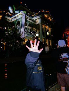 a person with their hand up in front of a large building at night, making the vulcan sign