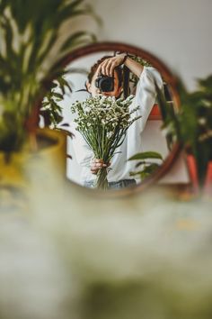 a woman taking a photo of herself in the mirror with her camera and some flowers