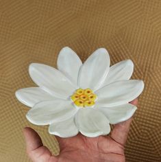 a hand holding a white ceramic flower with yellow stamens on it's center