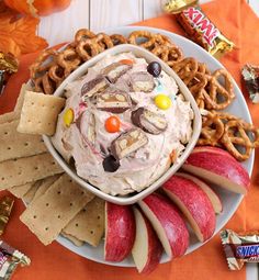 an apple pie dip surrounded by pretzels, crackers and candy on a plate