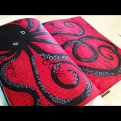 an open book with black and red octopus designs on it, sitting on a table