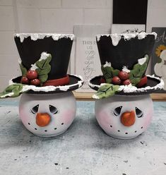 two snowmen with hats and holly leaves on their heads are sitting side by side