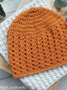 an orange and white crochet hat sitting on top of a wooden board next to a potted plant