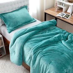 a bed with a turquoise comforter and pillows on it in a bedroom next to a book shelf