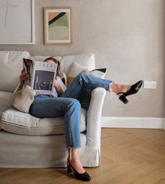 a woman sitting on a couch with her legs crossed, reading a book and wearing high heels