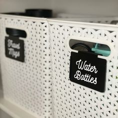 two white baskets with black labels on them and some scissors in the bottom one is labeled water bottles