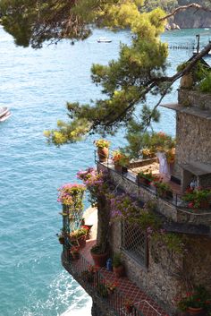 a balcony with flowers and potted plants on the side of a cliff next to water