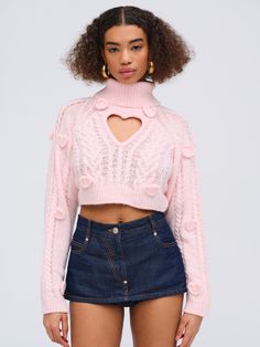 a woman wearing a pink sweater and denim skirt with cutouts on the shoulders, standing in