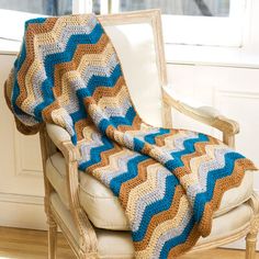 a crocheted blanket sitting on top of a white chair next to a window