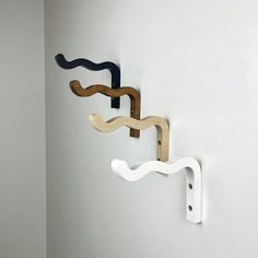 three wooden wall hooks mounted to the side of a white wall, one with two wavy designs on it