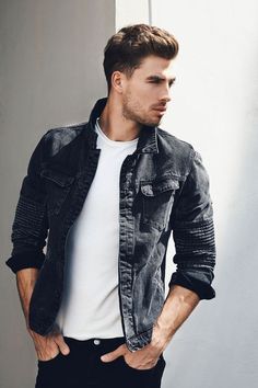 a young man wearing a denim jacket and white t - shirt is leaning against a wall