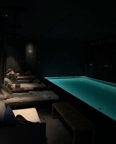 an indoor swimming pool at night with lounge chairs and pillows on the floor next to it