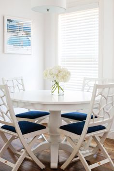 a white table with four chairs around it and a vase on top of the table