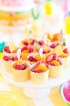 small cups filled with fruit on top of a white cake plate next to yellow plates