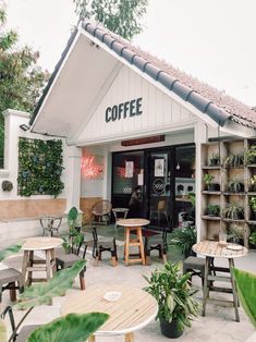 the outside of a coffee shop with tables, chairs and potted plants on display