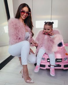 a woman in white pants and pink fur coat sitting on top of a toy car