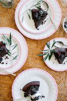 three slices of chocolate cake on plates with berries and rosemary garnish, one slice has been eaten