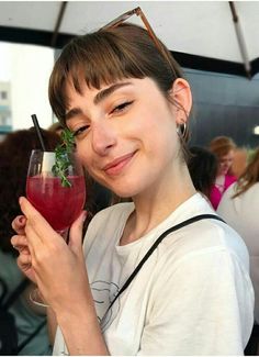 a woman holding a wine glass with a garnish on it's rim