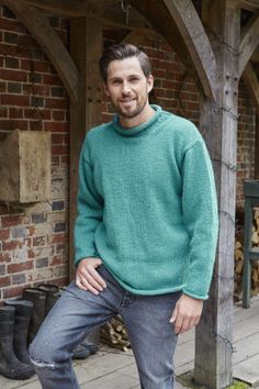 a man standing in front of a brick building wearing a green sweater and blue jeans