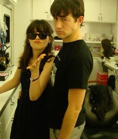 a man standing next to a woman in a kitchen wearing sunglasses and making the v sign with her hand