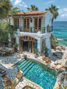 a house with a pool in front of it next to the ocean and palm trees