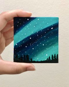 a hand holding up a piece of art that looks like an aurora bore in the sky