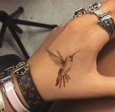 a woman's wrist with a small bird tattoo on the left side of her arm