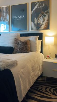 a white bed topped with lots of pillows next to two framed pictures on the wall