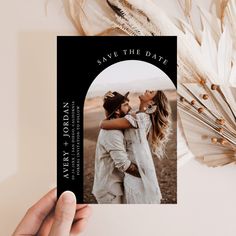 a hand holding up a save the date card with an image of two people kissing