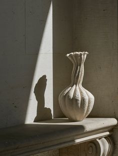 a white vase sitting on top of a shelf next to a window sill with the sun shining through it