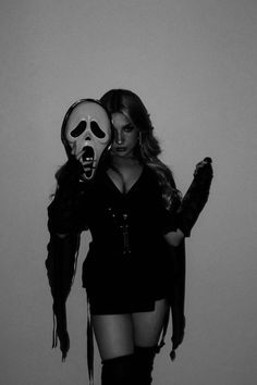 a woman wearing a skeleton mask and holding a knife in front of her face while standing against a wall