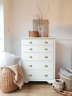 a white dresser sitting next to a basket on top of a wooden floor