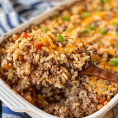 a casserole dish filled with rice, ground beef and green onions is being held by a wooden spoon