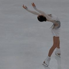 a female figure skating on the ice in a white dress and silver shoes with her arms outstretched