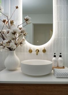 a bathroom sink with a mirror above it next to a vase filled with white flowers