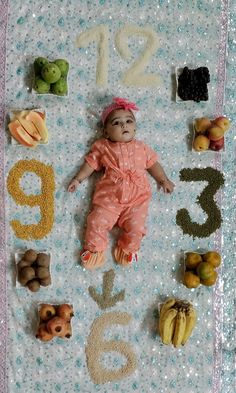 a baby laying on top of a blanket covered in fruits and vegetables next to numbers