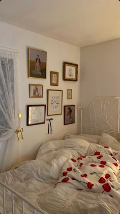 an unmade bed with white sheets and pictures on the wall