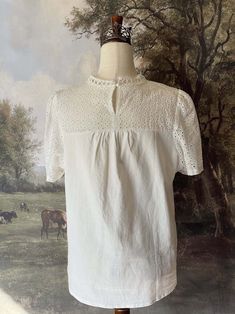 A charming historically inspired blouse that can be used in outfits ranging from the Edwardian era to the 1960's! This piece features a dainty eyelet lace yoke, scalloped lace mock-neck collar, short sleeves, and a gathered bodice. A versatile choice for building your historical wardrobe. This piece is part of our sustainable Secondhand, Vintage, and Upcycled Collection, and thus stock is limited to one! Sizing: Tag size XL, Fits like an XL.Bust up to 44 Inches / 110 CentimetersWaist up to 44 Inches / 110 CentimetersLength - 24.5 / 62 CentimetersSleeve Length - 8 / 22 CentimetersSleeve Width - 8 Inches / 22 Centimeters Condition: B | Some feeling of use, no major flaws. Materials: 100% Polyester synthetic "linen." Eyelet Blouse, Eyelet Lace, Curated Vintage, Scalloped Lace, Medieval Fashion, Edwardian Era, Baroque Fashion, Edwardian Fashion, Neck Collar