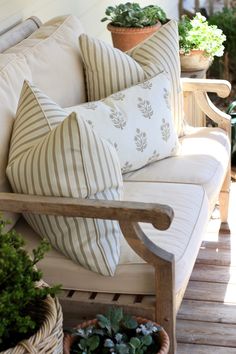 a couch with pillows and some plants on the back porch area in front of a house