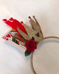 a gold crown with red feathers and a rose on the side, sitting on top of a card