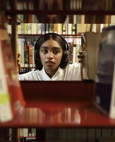 a girl with headphones on looking at the camera in front of bookshelves