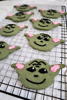 some green cookies with black and pink decorations on a cooling rack next to each other