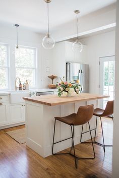 a kitchen island with two stools in front of it and flowers on the counter