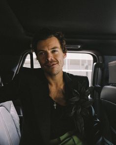 a man sitting in the back seat of a car wearing a black jacket and green shirt