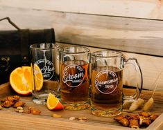 three glass mugs filled with liquid sitting on top of a wooden tray next to sliced oranges