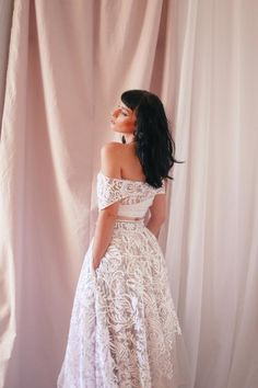 a woman wearing a white dress standing in front of a pink curtain with her back to the camera