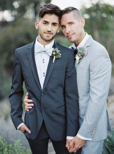 two men in suits standing next to each other with their arms around one another and looking at the camera