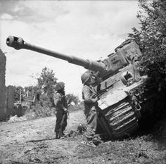 two men standing next to a tank in the dirt