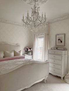 a white bedroom with chandelier, bed and dresser in the middle of it