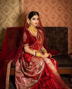 a woman in a red and gold bridal gown sitting on a couch with her hands clasped